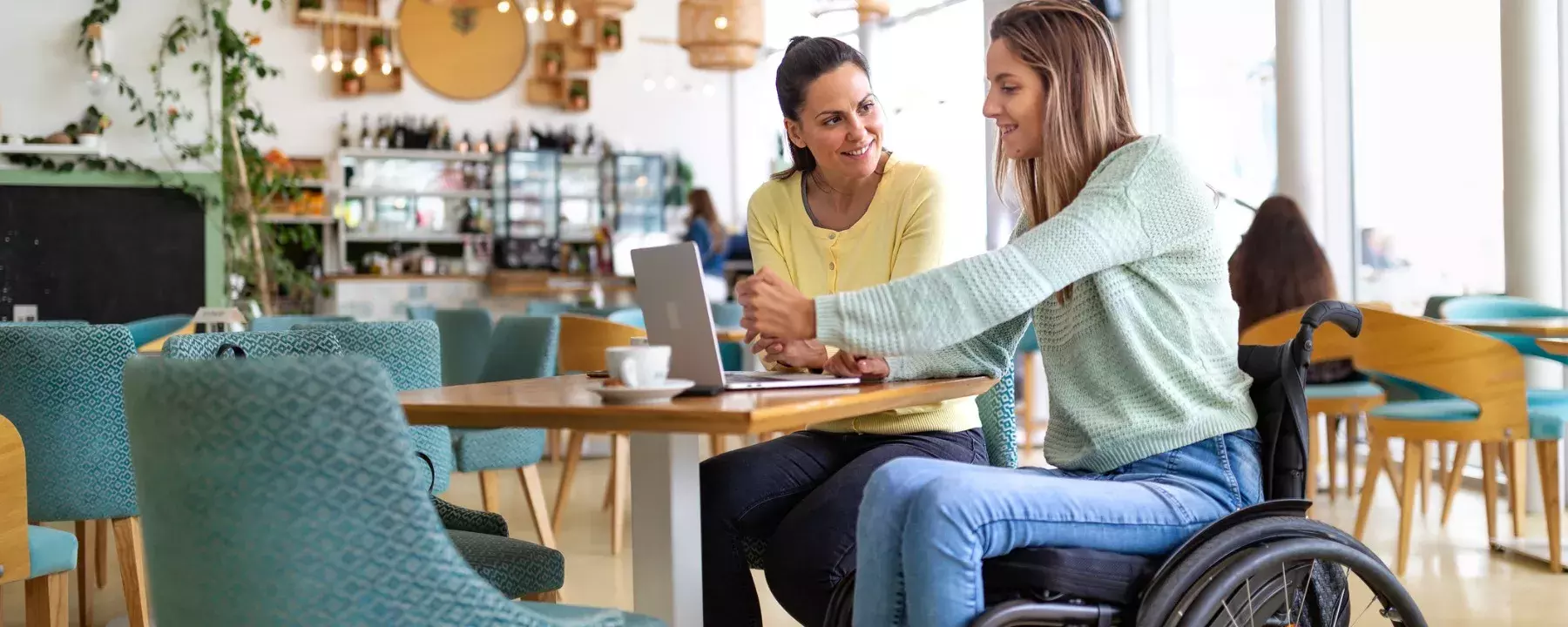 Healthcare-Young disabled woman shopping online in cafe with friend